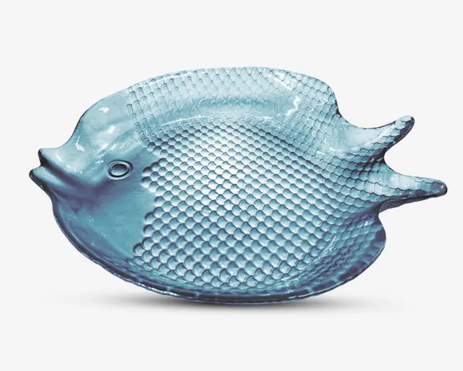En gennemsigtig, lyseblå glasskål formet som en fisk med et tekstureret skælmønster på kroppen, hævet hale og detaljeret ansigt med indtrykt øje. Skålen har en blank overflade og en let buet form, velegnet til servering eller dekoration.