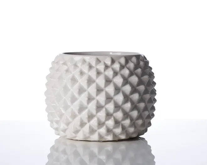 Rund, hvid keramisk beholder med blank overflade og et markant geometrisk, diamantmønstret tekstur. Siderne er dækket af hævede, pyramideformede knopper, hvilket giver et moderne og taktilt udtryk. Åbningen er bred og cirkulær, og formen er let lav og cylindrisk.