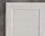 Nærbillede af et rektangulært tekstilprodukt med et tekstureret, vævet midterpanel og en bred, ensfarvet kant. Stoffet er råhvidt eller lysebeige, og kanten har en lidt højere luv end midten, hvilket giver en diskret kontrast i tekstur. Syningen langs kanten er pæn og forstærker kanten.