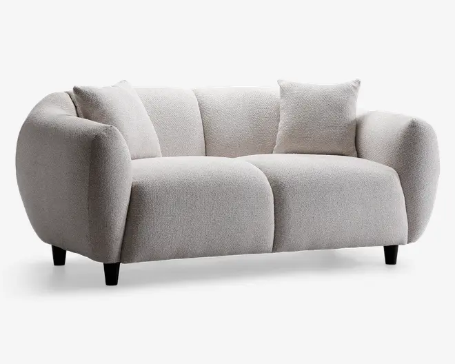 Moderne sofa med blød, tekstureret lysebeige polstring. Har afrundede, kraftigt polstrede armlæn og ryglæn, der giver et hyggeligt og indbydende udtryk. Inkluderer to matchende firkantede puder for ekstra komfort. Sofaen står på korte, koniske sorte ben, hvilket giver et moderne og solidt udseende.