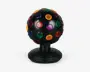 Sort kugleformet enhed med mat overflade, udstyret med flere runde, gennemsigtige linser i rød, grøn, gul, lilla og blå, jævnt fordelt over hele overfladen. Kuglen er monteret på en solid, facetslebet sort fod med en lille tænd/sluk-knap og er designet til at rotere og projicere farverige lys, når den er i brug.