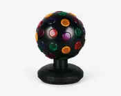 Sort kugleformet enhed med mat overflade, udstyret med flere runde, gennemsigtige linser i rød, grøn, gul, lilla og blå, jævnt fordelt over hele overfladen. Kuglen er monteret på en solid, facetslebet sort fod med en lille tænd/sluk-knap og er designet til at rotere og projicere farverige lys, når den er i brug.