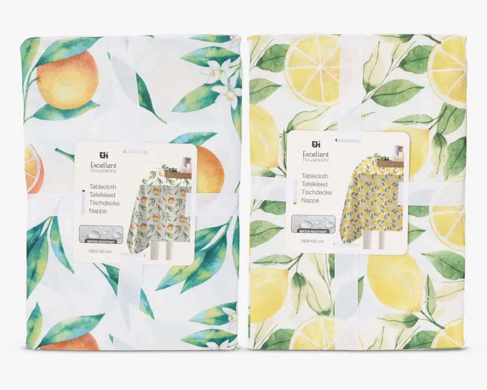 To sammenfoldede stofgenstande med farverige frugt-motiver. Den til venstre har appelsiner og grønne blade på hvid baggrund, samt små hvide blomster. Den til højre viser gule citroner, citronskiver og grønne blade, også på hvid baggrund. Begge er pænt pakket ind med et hvidt bånd og et produktmærke, der viser et eksempel på det fulde design.