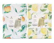 To sammenfoldede stofgenstande med farverige frugt-motiver. Den til venstre har appelsiner og grønne blade på hvid baggrund, samt små hvide blomster. Den til højre viser gule citroner, citronskiver og grønne blade, også på hvid baggrund. Begge er pænt pakket ind med et hvidt bånd og et produktmærke, der viser et eksempel på det fulde design.