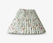 Plisseret lampeskærm med hvid baggrund og et fint blomstermønster i forskellige farver, herunder grønne blade samt røde, lilla og orange blomster. Plisseringen giver en tekstureret og tredimensionel effekt, og blomstermotivet er jævnt fordelt over hele overfladen.