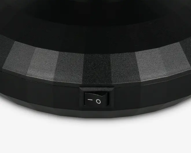 Nærbillede af en sort, facetslebet overflade med mat finish, der har en lille rektangulær tænd/sluk-vippeknap indbygget i siden. Kontakten er mærket med standard strømsymboler (en streg og en cirkel).