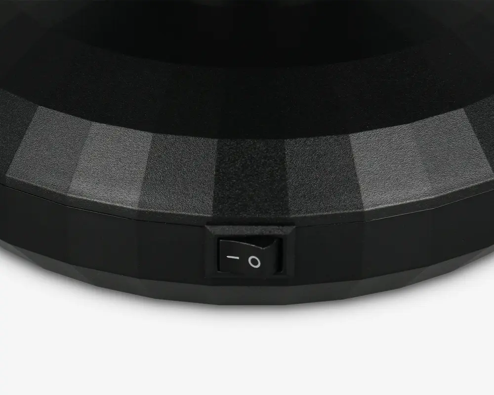 Nærbillede af en sort, facetslebet overflade med mat finish, der har en lille rektangulær tænd/sluk-vippeknap indbygget i siden. Kontakten er mærket med standard strømsymboler (en streg og en cirkel).