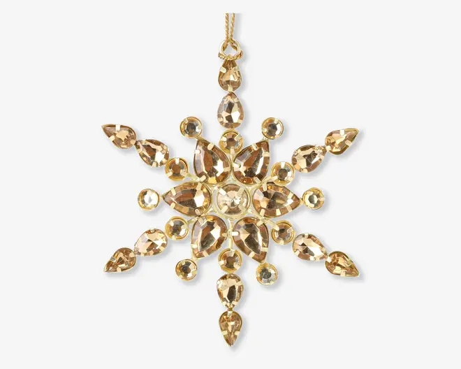 Guldfarvet ornament formet som en snefnug, dekoreret med flere facetslebne, dråbeformede og runde klare krystaller, der er arrangeret symmetrisk. Krystallerne sidder i en ramme af guldfarvet metal, hvilket giver et funklende og elegant udtryk. Øverst er der en lille løkke til ophængning.