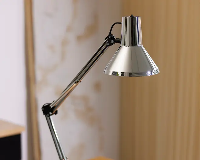 Justerbar skrivebordslampe med blank kromfinish, konisk lampeskærm og ledarm med synlige samlinger for fleksibel placering. Lampen har et slankt, moderne design og er velegnet til arbejdsbelysning.