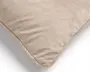 Nærbillede af en beige velourpude med blød, luftig struktur og en pænt kantbåndsafsluttet afrundet hjørne.