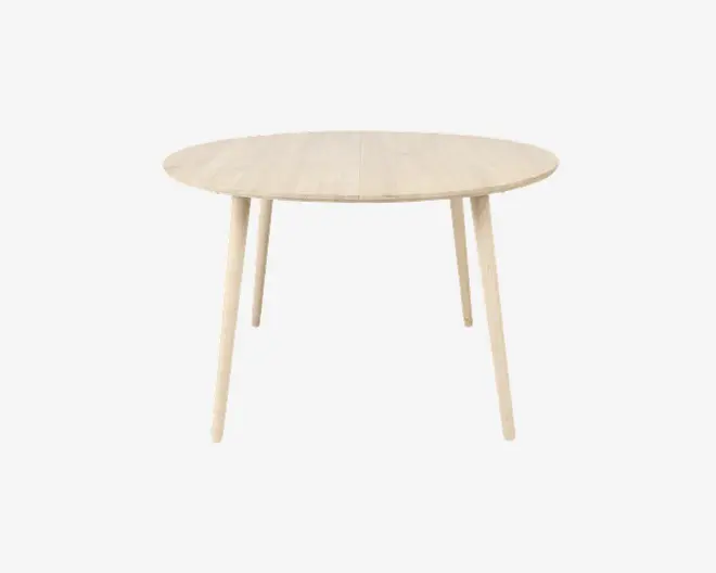 Et rundt bord med en lys træfinish, glat overflade og fire let skrå, tilspidsede ben. Bordet har et minimalistisk, skandinavisk-inspireret design med rene linjer og synlig træstruktur på overfladen.