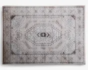 Rektangulært tæppe med et centralt diamantformet mønster og indviklede geometriske detaljer i nuancer af beige, brun og lysegrå. Kanten er dekoreret med små blomster- og abstrakte motiver, og hjørnerne har detaljerede trekantede accenter. Tæppet har et vintage-inspireret udtryk med en let slidt finish, der giver et blødt og afdæmpet udseende.