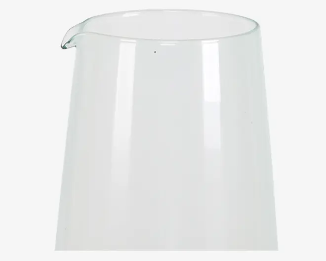 Klar glasbeholder med bred cylindrisk form, glat overflade og en lille hældetud. Glasset er gennemsigtigt og har en let udadgående kant foroven.