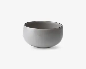 En rund, glat keramikskål med mat lysegrå yderside og en lidt mørkere inderside. Skålen har et minimalistisk design med blødt buede sider og en bred åbning, velegnet til servering af supper, salater eller snacks.