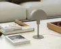 En lille, moderne bordlampe med mat taupe-finish. Lampen har en kuppelformet skærm og en slank, cylindrisk stang, der er fastgjort til en rund, flad fod. Designet er minimalistisk og nutidigt, velegnet til et skrivebord eller et sidebord. Lampen har en strømledning, der går ud fra bunden.