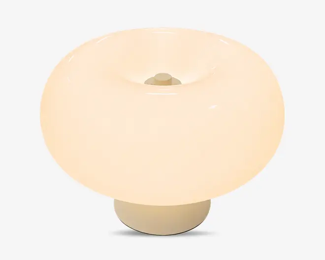 Blank, cremefarvet, rund lampe med en bred kuppelformet skærm, en fordybet åbning i midten og en kort cylindrisk fod.