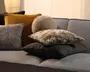 Assorterede pyntepuder i sennepsgul, grå, beige og sort med en blanding af velour, vævet stof, kunstpels og mønstrede teksturer, stablet på en lysegrå sofa.