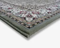 Nærbillede af et tæppehjørne, der viser en tyk, blød kant og detaljerede vævede mønstre. Designet har indviklede blomster- og geometriske motiver i nuancer af creme, rød, grøn og sort med en dekorativ kant. Tæppet ser ud til at have en tæt luv og en robust konstruktion.