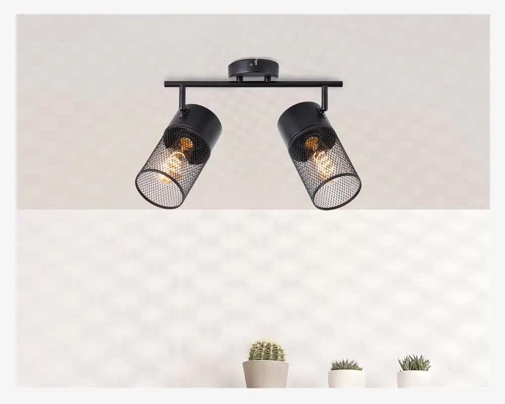 Loftmonteret lampe med to justerbare cylindriske lampeskærme, hver med et sort metalnet. Pærerne er synlige gennem nettet, hvilket giver et industrielt og moderne udtryk. Lampen er fastgjort til en rund base og en vandret stang, så lampeskærmene kan vinkles i forskellige retninger.