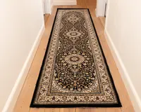 Et langt, smalt tæppe med et traditionelt persisk-inspireret design, der har en mørk bund med indviklede blomster- og vinmønstre i beige, creme og bordeaux. Tæppet har tre store, cirkulære medaljoner jævnt fordelt langs længden og en detaljeret kant med gentagne motiver. Kanterne er afsluttet med sort kantbånd, og tæppet ser ud til at have en lav luv, der egner sig til områder med meget trafik, såsom gange.