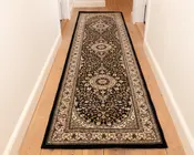 Et langt, smalt tæppe med et traditionelt persisk-inspireret design, der har en mørk bund med indviklede blomster- og vinmønstre i beige, creme og bordeaux. Tæppet har tre store, cirkulære medaljoner jævnt fordelt langs længden og en detaljeret kant med gentagne motiver. Kanterne er afsluttet med sort kantbånd, og tæppet ser ud til at have en lav luv, der egner sig til områder med meget trafik, såsom gange.