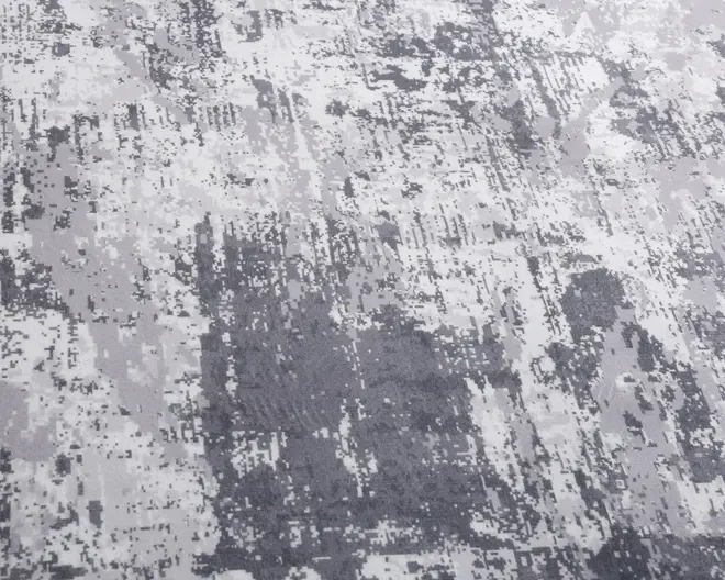 Overfladen har et abstrakt, pixeleret mønster i forskellige nuancer af grå og hvid. Designet har et moderne, slidt udtryk med uregelmæssige felter og spredte blokke, hvilket giver et tekstureret og dynamisk visuelt udtryk. Materialet ser blødt og behageligt ud, velegnet til moderne indretning.