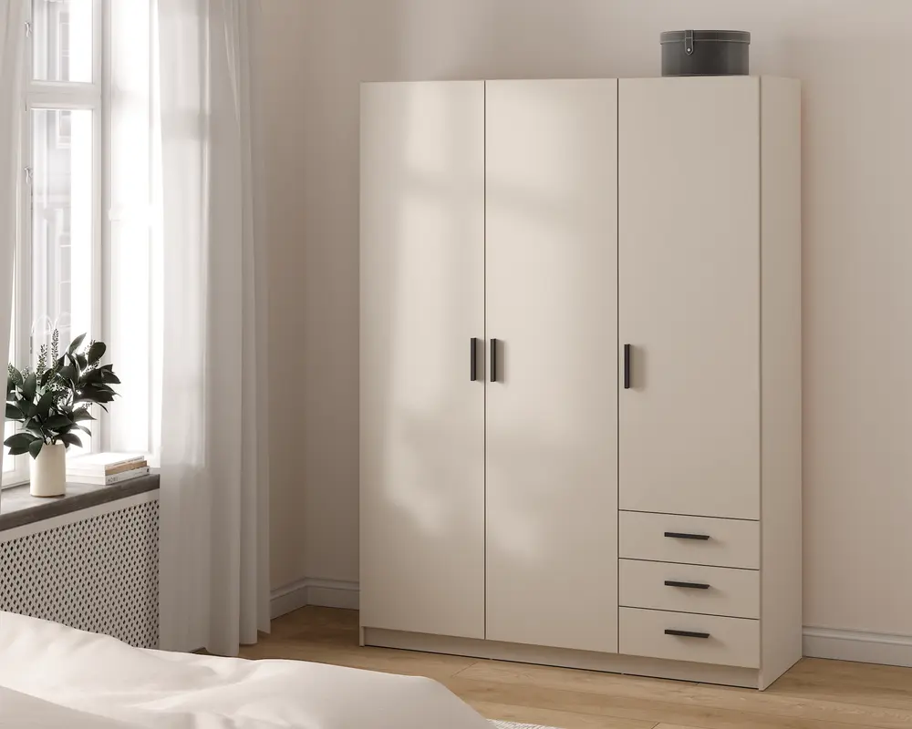 Et moderne, fritstående garderobeskab i en lys beige farve med et minimalistisk design. Skabet har tre høje låger med slanke, mørke greb og tre rummelige skuffer i højre side, alle med matchende greb. Overfladen er glat og mat, og skabet står på en flad sokkel. Øverst står en rund opbevaringsboks. Udtrykket er enkelt og moderne, velegnet til et soveværelse med neutrale farver.