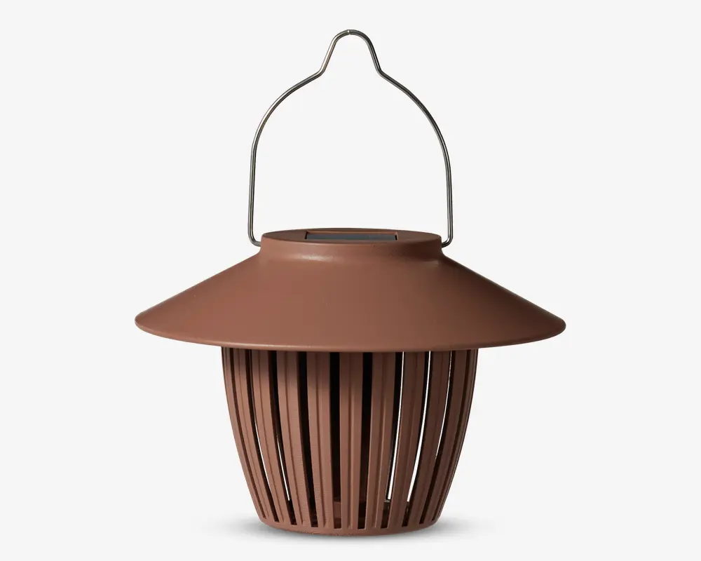 En brun lanterne med en bred, skrånende top og lodrette lameller, der udgør kroppen og lader lyset passere igennem. Den har et robust metalhåndtag til ophængning og en glat, mat overflade. Designet er moderne og minimalistisk, velegnet til både indendørs og udendørs brug.