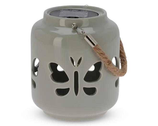 En rund, lysegrå lanterne af keramik med udskårne sommerfugleformer på siderne, som lader lyset skinne igennem. Lanternen har et kraftigt, flettet rebhåndtag fastgjort med metalbeslag, så den nemt kan bæres eller hænges op. Toppen har et forsænket område, sandsynligvis til et stearinlys eller LED-lys.