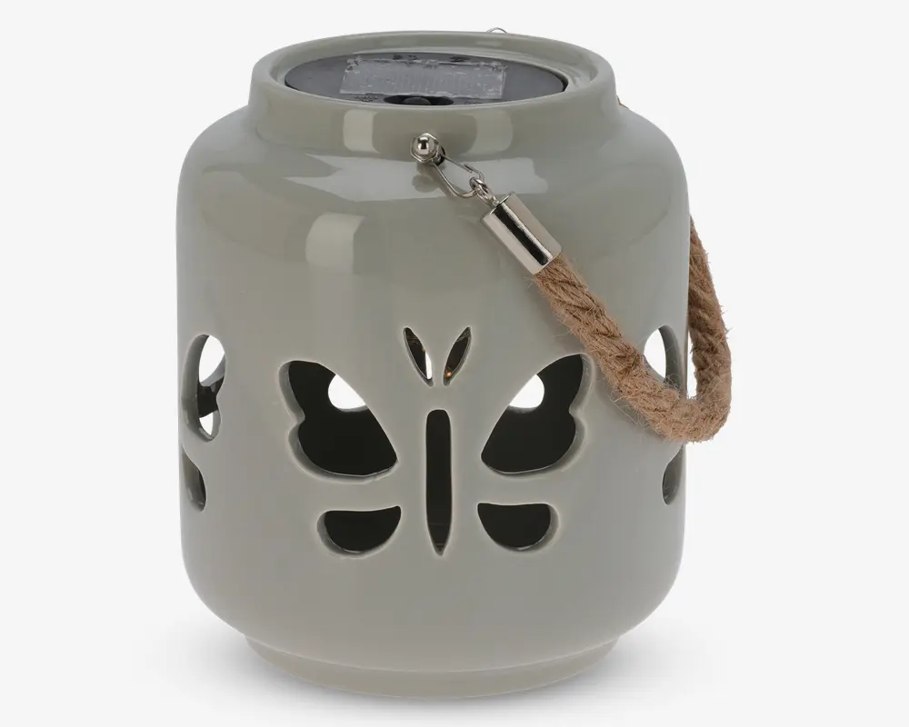 En rund, lysegrå lanterne af keramik med udskårne sommerfugleformer på siderne, som lader lyset skinne igennem. Lanternen har et kraftigt, flettet rebhåndtag fastgjort med metalbeslag, så den nemt kan bæres eller hænges op. Toppen har et forsænket område, sandsynligvis til et stearinlys eller LED-lys.