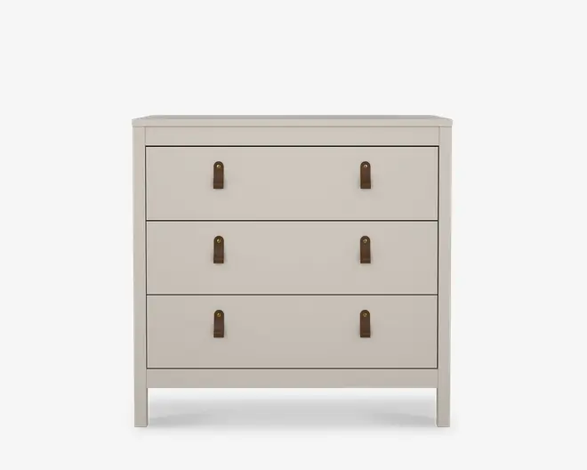 En kommode med tre skuffer i en glat, mat lysebeige finish. Hver skuffe har to lodrette brune lædergreb med messingdetaljer, hvilket giver et moderne og varmt udtryk. Designet er enkelt og rektangulært med rene linjer og let tilspidsede ben for et moderne look.
