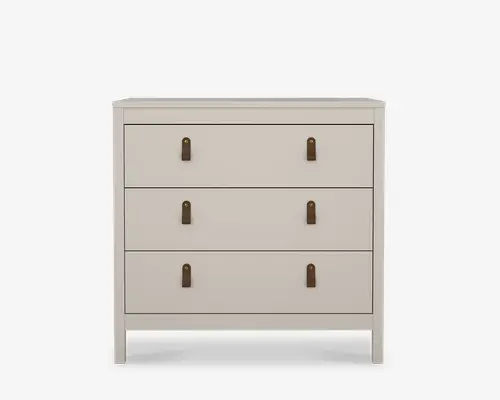 En kommode med tre skuffer i en glat, mat lysebeige finish. Hver skuffe har to lodrette brune lædergreb med messingdetaljer, hvilket giver et moderne og varmt udtryk. Designet er enkelt og rektangulært med rene linjer og let tilspidsede ben for et moderne look.