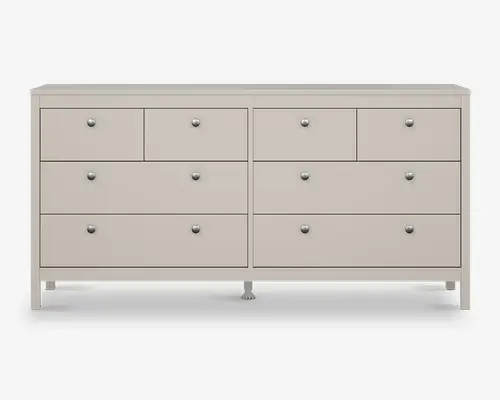 En bred, lysegrå kommode med seks rummelige skuffer fordelt i to kolonner. Hver skuffe har en enkel, rund metalgreb for nem åbning. Kommoden har et rent, moderne design med lige kanter og en glat overflade, og den står på korte, solide ben.