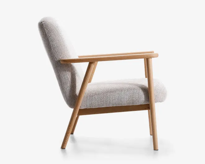 Sidebillede af en moderne lænestol med lysebeige tekstureret stofpolstring. Stolen har et minimalistisk design med en let skråtstillet ryg og sæde for komfort. Stel, ben og armlæn er lavet af lyst træ med rene linjer og en naturlig finish. Armlænene er lige og let hævede, hvilket giver støtte. Det samlede udtryk er stilrent og moderne, velegnet til stue eller lounge.