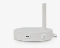 Et nærbillede af basen på en moderne, hvid skrivebordslampe. Basen er rund med en mat overflade og har en USB-C opladningsport samt en tænd/sluk-knap på siden. Lampens stang er slank og lodret og er fastgjort til kanten af basen. Bunden af basen er sort, hvilket giver en kontrast til den hvide overdel.