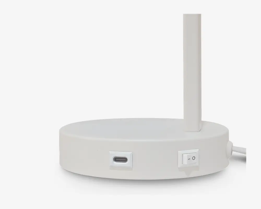 Et nærbillede af basen på en moderne, hvid skrivebordslampe. Basen er rund med en mat overflade og har en USB-C opladningsport samt en tænd/sluk-knap på siden. Lampens stang er slank og lodret og er fastgjort til kanten af basen. Bunden af basen er sort, hvilket giver en kontrast til den hvide overdel.