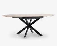 Ovalt bord med en lys, glat bordplade og en markant sort metalbase, der består af flere skråtstillede ben, som mødes i midten og giver et moderne, skulpturelt udtryk. Bordet ser ud til at have en udtræksfunktion, så der kan skabes ekstra plads til gæster.