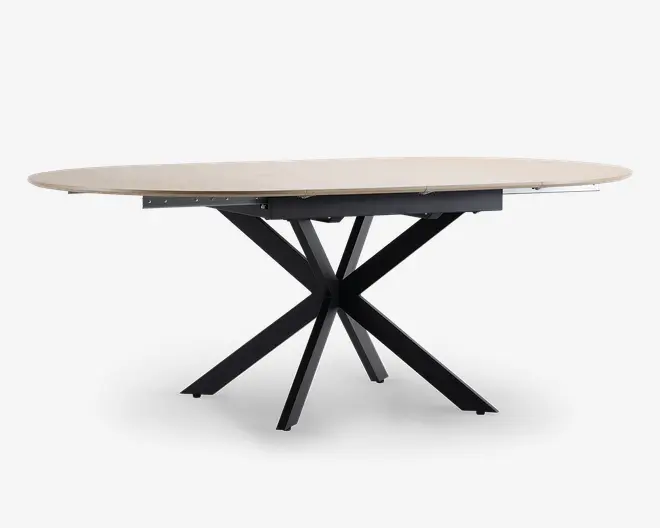 Ovalt bord med en lys, glat bordplade og en markant sort metalbase, der består af flere skråtstillede ben, som mødes i midten og giver et moderne, skulpturelt udtryk. Bordet ser ud til at have en udtræksfunktion, så der kan skabes ekstra plads til gæster.