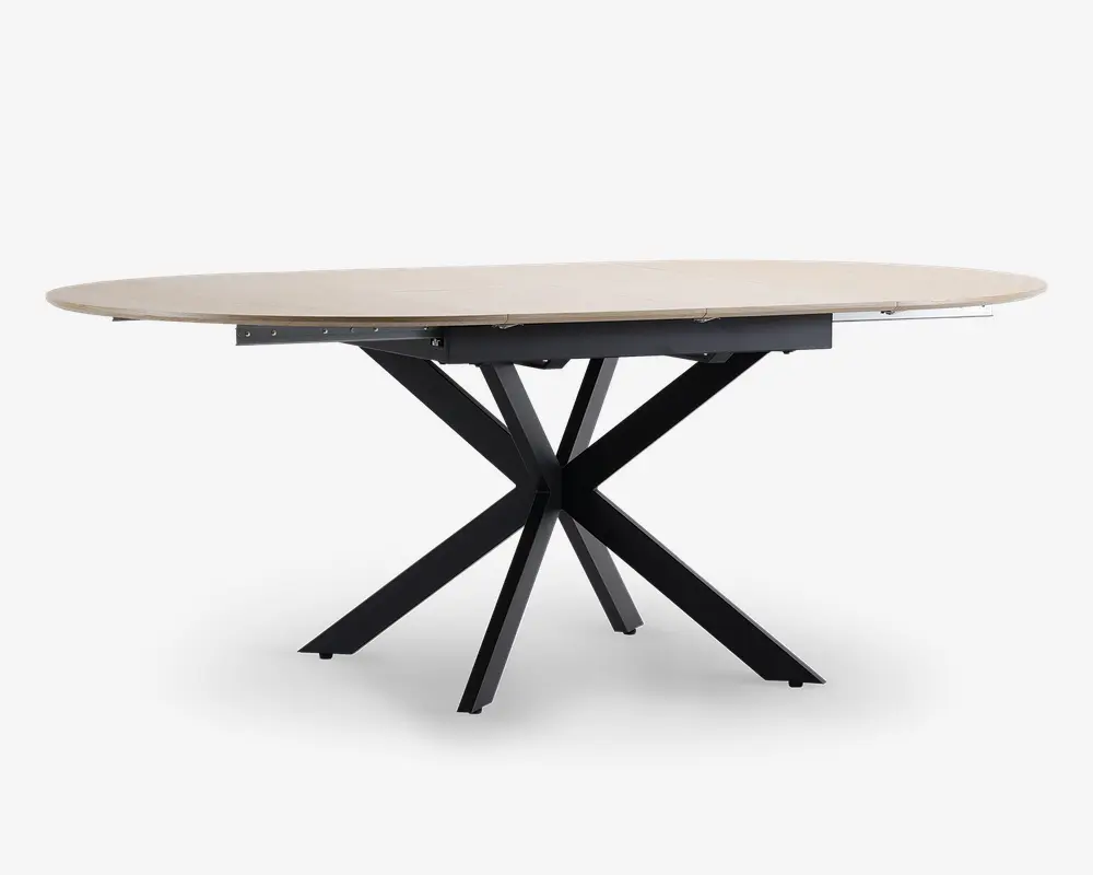 Ovalt bord med en lys, glat bordplade og en markant sort metalbase, der består af flere skråtstillede ben, som mødes i midten og giver et moderne, skulpturelt udtryk. Bordet ser ud til at have en udtræksfunktion, så der kan skabes ekstra plads til gæster.