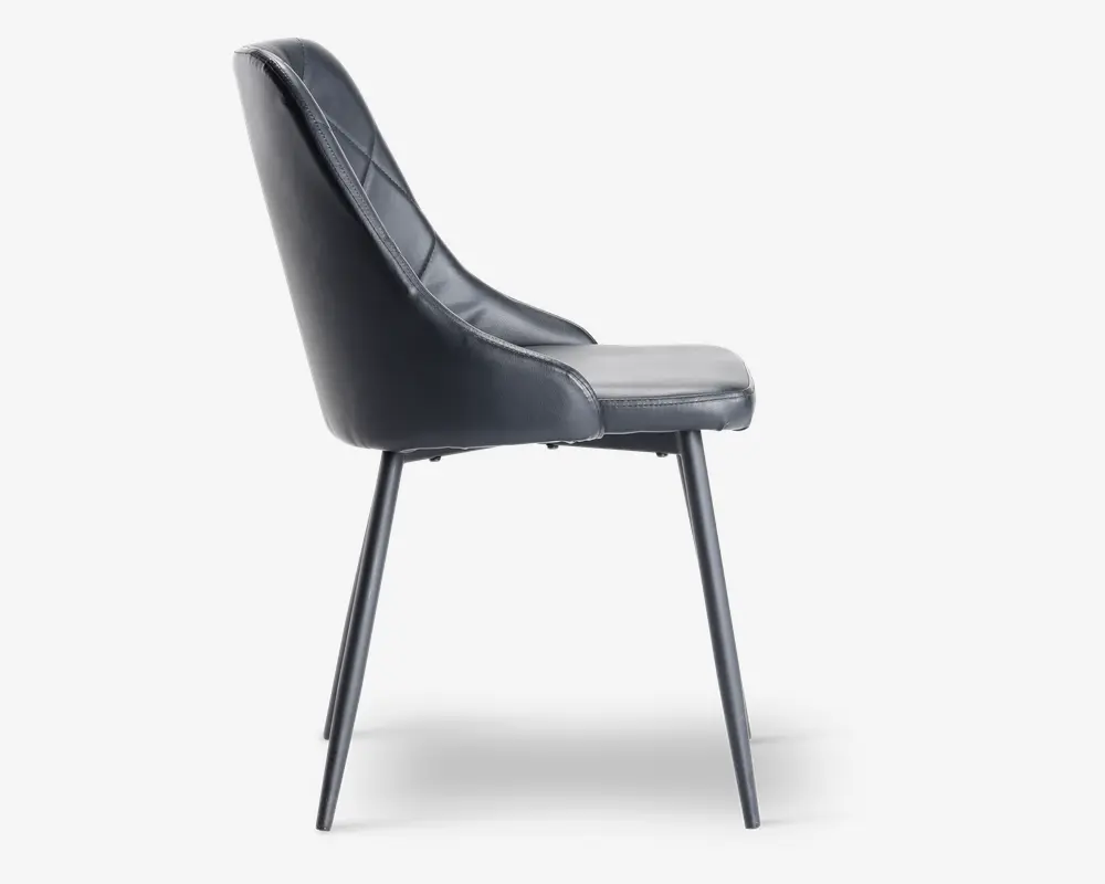 Sidevisning af en moderne stol med sort kunstlæderbetræk og diskrete syninger. Stolen har et let buet ryglæn for ergonomisk støtte og en polstret siddeflade for komfort. Den står på fire slanke, skråtstillede metalben med mat sort finish, hvilket giver et stilrent og minimalistisk udtryk.