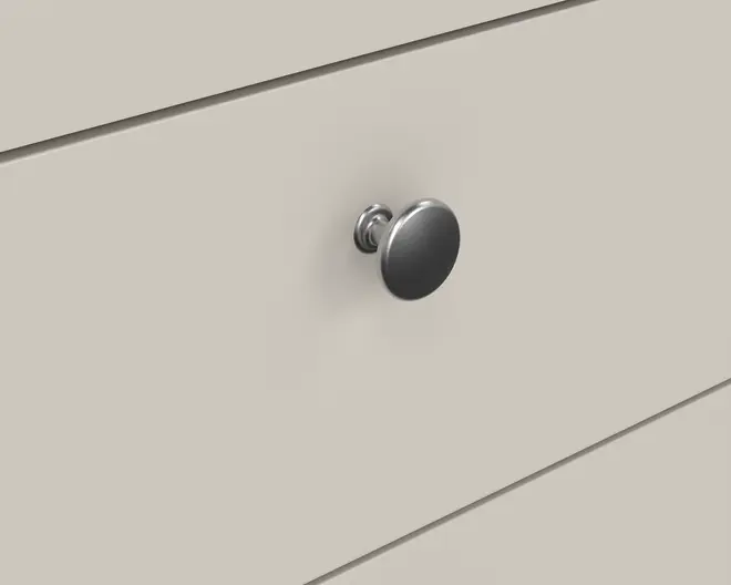 Nærbillede af en glat, rund metalgreb med børstet finish, monteret på en flad, lysebeige overflade. Grebet har et enkelt, klassisk design med en let forhøjet base, hvilket giver et godt greb til at åbne og lukke skuffer eller skabe.