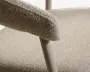 Nærbillede af et sæde betrukket med beige boucle-stof med afrundet polstret armlæn og et slankt, lys beige metalben.