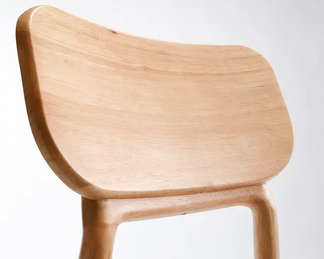 Nærbillede af stolens ryglæn og øverste stel, fremstillet af lyst, glatpoleret træ. Ryglænet har en let buet, ergonomisk form for komfort, med afrundede kanter og en sømløs overgang til stellet. Træets åretegning er synlig og giver et naturligt og minimalistisk udtryk.