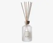 Frostet glasflaske med trælåg, der indeholder flere naturfarvede duftpinde. Flasken har minimalistisk sort tekst på forsiden, herunder ordene 'SOFT LINEN.' Det samlede design er enkelt og elegant, velegnet til moderne boligindretning.
