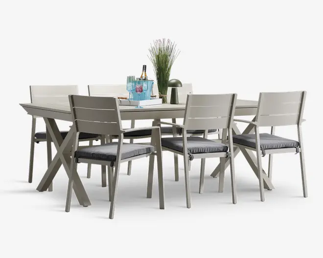 Et moderne spisesæt bestående af et rektangulært bord med lys grå finish og seks matchende stole. Stolene har lamelrygge og armlæn samt grå sædehynder for ekstra komfort. Bordet har solide, skråtstillede ben for stabilitet. På bordpladen står en dekorativ opstilling med en vase med blomster, et fad med blå glas og en lille grøn lampe, hvilket giver et elegant udtryk til sættet.