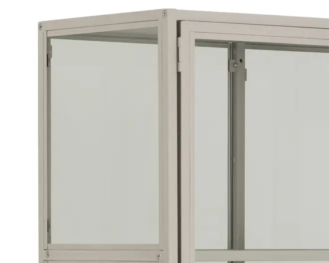 Nærbillede af det øverste hjørne af et vitrineskab med en solid, lysegrå metalramme og klare glasplader på siderne og fronten. Skabet har rene, lige kanter og synlige metalbeslag i hjørnerne, hvilket giver det et moderne og minimalistisk udseende.