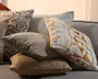 En stak dekorative pyntepuder på en grå sofa, herunder en pude med blomsterprint, en ensfarvet taupe pude, en struktureret beige pude og en creme- og orange geometrisk pude foran.