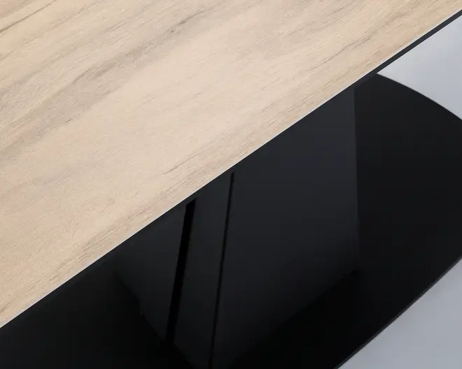 Nærbillede af en bordplade med lyst trælook og en solid sort base. Overfladen er glat med naturlige træmønstre, og basen har en blank, reflekterende finish, hvilket giver et moderne og elegant udtryk.