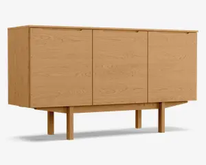 Rektangulært skab i træ med naturlig egetræsfinish, udstyret med tre flade låger med diskrete, integrerede greb øverst. Skabet står på fire solide, firkantede ben, der er forbundet af en vandret støttebjælke, hvilket giver et hævet og stabilt udtryk. Træets årer er synlige på alle flader og tilfører struktur og varme til det minimalistiske design.