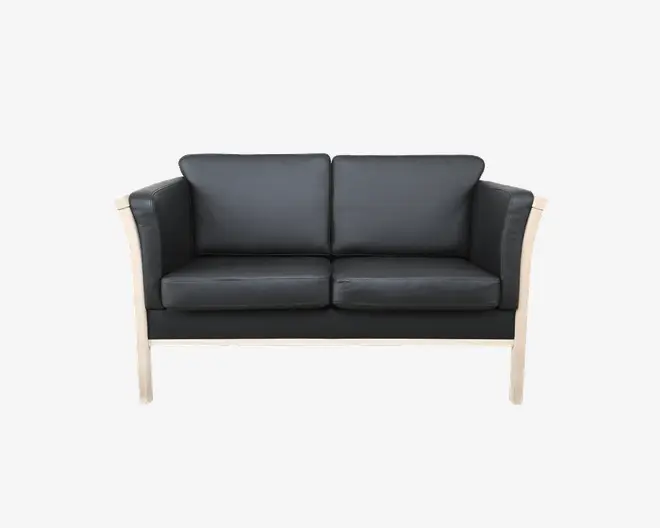 To-personers sofa med sorte læderhynder og en lys træramme. Sofaen har lige armlæn og ryglæn samt tykke, aftagelige sæde- og ryghynder for ekstra komfort. Designet er moderne og minimalistisk, hvor de synlige træben og rammen skaber en kontrast til det mørke betræk.